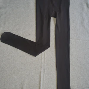 Svarta leggings i stretchigt material - Svarta leggings med bra passform och hög midja. Tillverkade i ett stretchigt syntetmaterial som sitter skönt mot kroppen. Perfekta att styla med oversized tröjor eller hoodies.