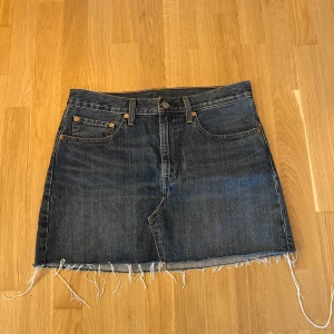 Levis kjol  - Jeans kjol från Levis, med rå kant nedtill och klassisk Levi's-stil. Den har fickor både fram och bak, samt en liten röd Levi's-etikett på bakfickan. Storlek 30. Fint skick. 