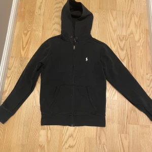 Ralph lauren zip hoodie - Klassisk zip hoodie från Ralph Lauren i svart färg med broderad logga på bröstet. Mjuk och skön bomullskvalitet, perfekt för vardagsbruk. 	•	Storlek: XS 	•	Nypris: ca 2000 kr (köpt på NK) 	•	Skick: Väldigt fint skick, sparsamt använd