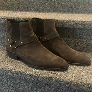 Svarta mocka boots - Säljer ett par mörkbruna boots i mocka från Bianco med dekorativt bälte och metallspännen runt ankeln. Skorna är bara använda några ensktaka gånger så är i väldigt bra skick! Storlek 46. 