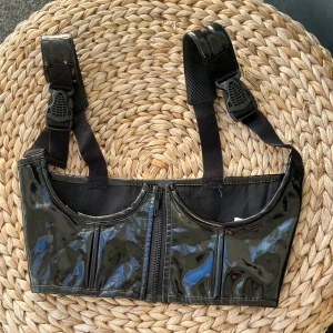 Svart lack korsett-topp från Poster Girl - Säljer en svart glansig underbust korsett-topp från Poster Girl/dollskill med dragkedja framtill och breda axelband med spännen. För en goth eller edgy look. Materialet är en mix av rayon och polyuretan med bomullsfoder.