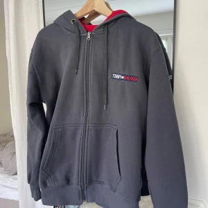 Tommy Hilfiger hoodie - Säljer en mörkgrå hoodie från Tommy Hilfiger med dragkedja framtill och huva med snörning. Tröjan har två stora fickor och broderad logga på bröstet. Perfekt för en avslappnad stil.