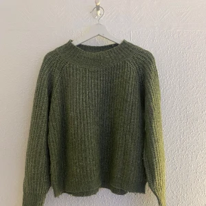 Olivgrön stickad tröja från 157 - Mysig olivgrön stickad tröja från 157 med grovstickad struktur och rund halsringning. Perfekt för lager-på-lager och passar till både jeans och kjol. Tröjan har långa ärmar och avslappnad passform.