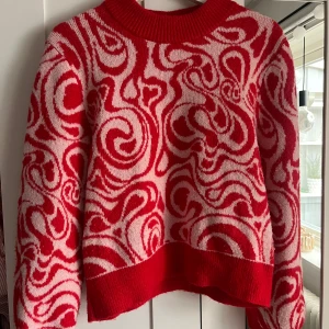 Röd och rosa mönstrad stickad tröja - Säljer en stickad tröja med unikt rödrösa mönster och bred ribbad mudd i hals och nederkant. Tröjan har lång ärm och är perfekt för dig som vill sticka ut med färg och mönster. Har använt till både jul, alla hjärtansdag och till vardags. Skriv för fler bilder❤️