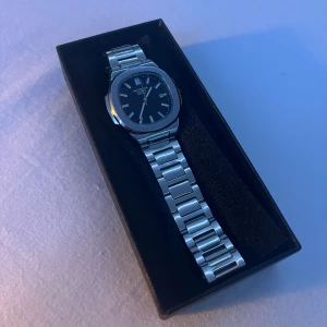 Silverfärgad klocka från Modaiya Quartz - Stilren klocka från Modaiya Quartz med svart urtavla och datumvisning. Armbandet är i silverfärgad metall och har en klassisk länkdesign. Urtavlan är rundad med tydliga index och visare, perfekt för dig som gillar en clean look.