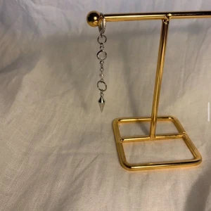 Silvrigt hängande örhänge med pärldetalj - Unikt hängande örhänge i silverfärg med flera ringar, en liten vit pärldetalj och en spetsig kon längst ner. Perfekt för dig som gillar edgy och stilrena accessoarer med en twist.