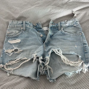 Ljusblå slitna jeansshorts - Ljusblå jeansshorts från Zara med låg midja och rejält slitna detaljer framtill. Råa kanter och fransar ger en riktigt edgy vibe. Klassisk fyrficksmodell i mjuk bomullsdenim, perfekt för sommaren.