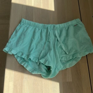 Mintgröna frottéshorts Hollister S - Supermjuka mintgröna shorts från Hollister i frotté med snörning i midjan och söt volangkant nedtill. Perfekta för varma dagar eller chilla hemma. Elastisk midja för skön passform och diskret metallogo framtill.