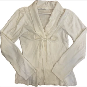 Vit kofta med knytband - Söt vit kofta med långa ärmar, knytband framtill och volang nertill. Skriv om ni har frågor eller vill ha bild hur den sitter på! 