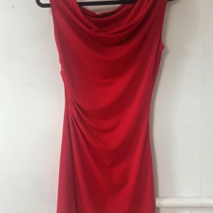 Röd draperad klänning från BikBok XS - Snygg röd klänning från BikBok i storlek XS. Draperad framtill med en cool cowlneck och lätt rynkade detaljer i sidan. Klänningen är ärmlös och har en figurnära passform, perfekt för dig som vill sticka ut. Materialet känns mjukt och följsamt.