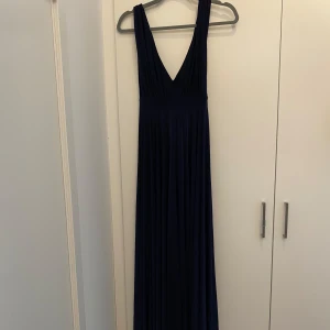 Mörkblå långklänning med v-ringning - Elegant mörkblå långklänning med djup v-ringning och breda axelband. Klänningen har ett markerat midjeband och ett mjukt, fallande tyg som ger ett snyggt flow. Dragkedja i sidan för enkel påklädning. Perfekt för dig som vill sticka ut med stil. Oklart med storleken men jag hade den när jag var mellan en s och m.