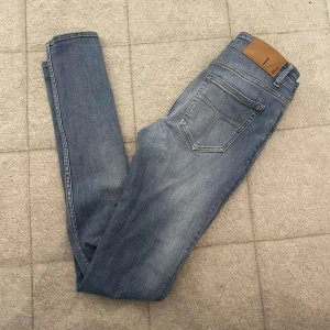 Tiger of sweden jeans  - Säljer ett par ljusblå slim jeans från tiger of sweden med klassisk femficksdesign och snygga slitningar. Jeansen har normal midja och är tillverkade i mjukt bomullsmaterial med lite stretch för extra komfort. Perfekta för dig som gillar en smal passform och stilren look.