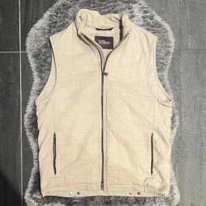 Oscar Jacobson Liner EVO Waistcoat Väst Beige - Stilren och mångsidig beige väst från Oscar Jacobson, modell Liner Evo Waistcoat. Ett perfekt mellanlager eller komplement till din höstlook.  Storlek 48 – motsvarar Medium Finns tecken på användning, men helhetsintrycket är fint