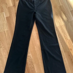 Svarta bootcut kostymbyxor med låg midja - Säljer ett par svarta kostymbyxor med bootcut-modell och låg midja. Byxorna har klassisk knapp- och dragkedjestängning och är i ett mjukt, stretchigt material som sitter snyggt över höfterna och låren. Perfekta om du gillar en stilren och enkel look.