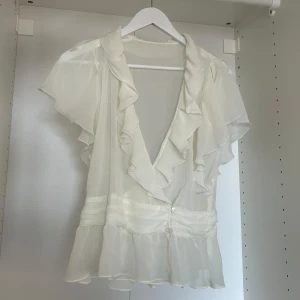Genomskinlig blus  - Vit blus som man knäpper med knappar. V-ringad med volanger. Såsåså söt men kommer ej till använding