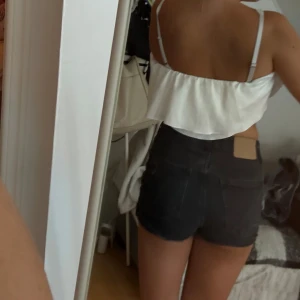 Svarta jeansshorts från H&M, strl 36 - Snygga svarta jeansshorts från H&M i storlek 36. Modellen är högmidjad med slitna detaljer och råa kanter för en cool vibe. Klassisk femficksdesign, dragkedja och knapp framtill. Perfekta till sommaren och lätta att matcha med allt.