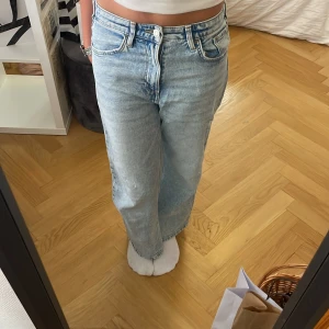 Ljusblå wide leg jeans H&M 146 - Säljer ett par ljusblå wide leg jeans från H&M i storlek 146. De har hög midja, justerbar midja och en liten sliten detalj på ena benet. Klassisk femficksmodell i mjuk bomullsdenim.
