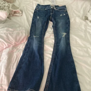 Blå bootcut jeans från Gina Tricot XS - Snygga blå bootcut jeans från Gina Tricot i storlek XS. Jeansen har slitna detaljer framtill, klassiska fickor och broderade bakfickor. De är tillverkade i jeansmaterial och har en cool, lite vintage vibe. Har andvent en gång 