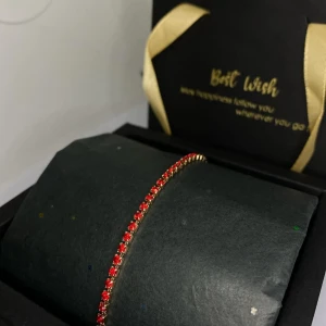 Guldfärgat armband med röda stenar - Ett smalt och elegant armband i guldfärg med gnistrande röda stenar i rad. Perfekt för dig som vill ha en färgklick på handleden och gillar stilrena smycken med lite extra bling. Ej använd utan kommer från min small business. 
