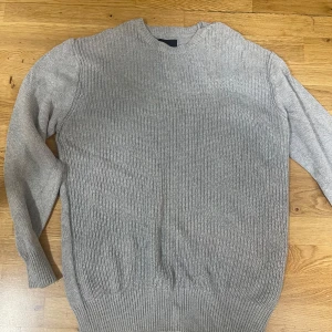 Grå stickad tröja från 157 XXL - Snygg grå stickad tröja från 157 i storlek XXL. Tröjan har en klassisk rund halsringning och ribbade muddar vid ärmslut och nederkant. Perfekt för lager-på-lager och chill dagar. Enkel att matcha med jeans eller chinos.
