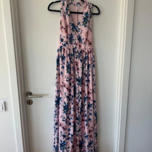 Lång blommig klänning i rosa och blått - Säljer en superfin långklänning med rosa botten och blått blommönster. Klänningen har v-ringning och är ärmlös. Dyrare då den var dyr!