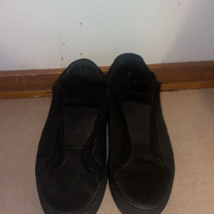 Svarta sneakers från Axel Arigato - Stilrena svarta sneakers från Axel Arigato i mocka med minimalistisk design. Skorna har låg profil, rund tå och platt sula. Perfekta för dig som gillar en clean look och vill ha ett par klassiska svarta sneakers i garderoben.