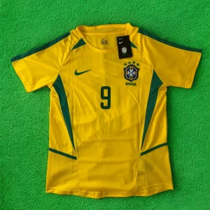 Brasilien Ronaldo 9 fotbollströja Nike - Gul Brasilien fotbollströja med gröna detaljer, nummer 9 och Ronaldo på ryggen. Officiell CBF-logga på bröstet och Nike Swoosh. Klassisk passform med korta ärmar, tillverkad i lätt och ventilerande material. Perfekt för dig som älskar fotboll och legendariska spelare.