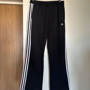 Svarta Adidas byxor med vita ränder - Oanvända tidlösa klassiska Adidas original byxor. Byxorna har elastisk midja och är tillverkade i 100% polyester. De har en rak och lite loose passform, sportig och avslappnad stil. Storleken är 38 men passar även 36/S .