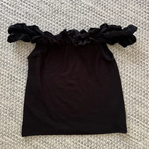Svart offshoulder topp med volang - Svart offshoulder topp från Cubus i storlek M. Toppen har bred volang längs axlarna som ger en snygg och trendig look. Perfekt till jeans eller kjol när du vill sticka ut lite extra. Mjuk och skön känsla.