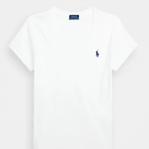 Vit v-ringad t-shirt från Polo Ralph Lauren - Klassisk vit t-shirt från Polo Ralph Lauren med v-ringning och korta ärmar. Tillverkad i mjuk bomull och prydd med den ikoniska blå loggan broderad på bröstet. Perfekt basic-plagg med clean look och skön passform.