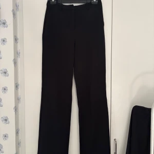 Svarta kostymbyxor från Vero Moda - Säljer ett par svarta kostymbyxor i storlek M/34 från Vero Moda! Jag är 176cm lång och dessa sitter bra på mig när jag har de i låg/medelhög midja.