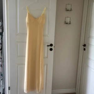 Ljusgul långklänning med smala axelband - Supersöt långklänning i ljusgul nyans med smala justerbara axelband. Klänningen har en figurnära passform upptill och faller rakt ner. Perfekt för varma dagar och ger en fräsch och somrig vibe. Aldrig använd
