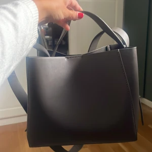 Mocca brun axelväska från Gina Tricot - Stilren mocca brun axelväska från Gina Tricot i slät skinnimitation. Väskan har en fyrkantig form, bred axelrem och ett stort huvudfack med innerficka som stängs med dragkedja. Perfekt för dig som gillar minimalistisk och clean look. Skriv om ni har frågor!