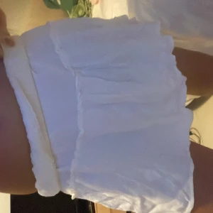 Vit volangkjol med resårmidja - Supersöt lowwaist vit kortkjol med volanger och resår i midjan. Kjolen har en flowy känsla och är perfekt för dig som gillar en luftig och lätt stil. Passar grymt till sneakers eller sandaler för en chill look.