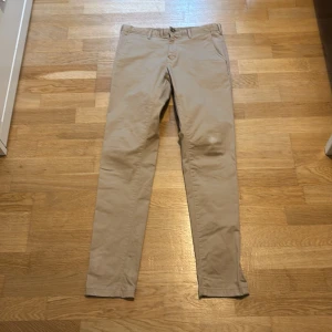 Beige Barton chinos super slim fit - Snygga beige chinos från Barton i super slim fit-modell. Byxorna är tillverkade i mjuk bomull med lite stretch för extra komfort. Klassisk design med fickor fram och bak samt dragkedja och knapp i midjan.