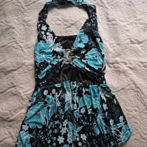 Blommig halterneck topp - Supersöt unik halterneck topp med blommigt mönster och fint spänne fram! Köpt secondhand, säljer för att den är lite stor för mig :) Står inte storlek men skulle uppskatta M. 