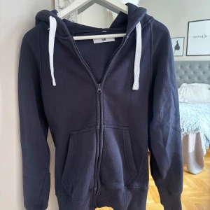 Mörkblå hoodie från Russemerch - Mörkblå hoodie från Russemerch med vit snörning i huvan och hel dragkedja framtill. Som man ser på bilderna så har den dels blivit lite missfärgad vid ärmen, blivit lite nopprig på insidan och så har tråden gått upp pyttelite på ärmen. Nypris: 750kr