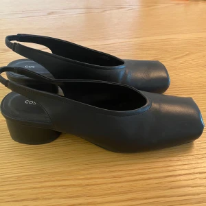 Svarta pumps med fyrkantig tå från COS - Svarta pumps / slip-ins / sling back-skor från COS i skinn med låg klack och öppen häl. Storlek 40, men lite små, så passar någon med storlek 39. Använda en gång inomhus.