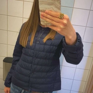 Marinblå jacka från Uniqlo - Säljer en mörkblå, quiltad lättviktsdunjacka från Uniqlo i storlek S. Jackan har knäppning framtill, rundad krage och är tillverkad i ett tunt, vattenavvisande material. Perfekt för lager-på-lager och enkel att bära med sig. Små defekter: Det är lite ludd som sticker ut på ena armen och på framsidan vilket man ser på de sista bilderna. Men detta är ingenting som syns och jackan är jätte fin ändå.