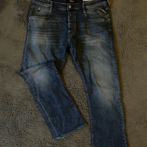 Blå Replay jeans straight fit - Säljer ett par klassiska blå jeans från Replay med snyggt slitna detaljer och raka ben. Jeansen har fem fickor, dragkedja och knapp framtill samt diskreta kontrastsömmar. Perfekta för dig som gillar en tidlös och avslappnad look.