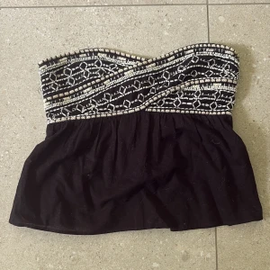 Svart tubtopp med broderi från Zara - Svart tubtopp från Zara med snyggt broderi och pärldetaljer upptill i vitt och beige. Toppen är bandeau-modell och har smockad rygg för skön passform. Perfekt för dig som vill sticka ut med coola detaljer och boho-vibe.🫶🏻💗