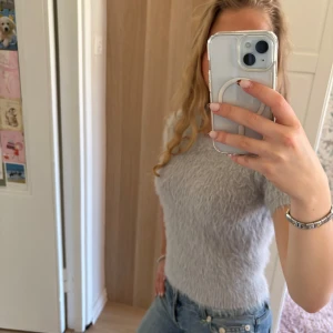 Ljusgrå fluffig kortärmad topp - Säljer en ljusblå, fluffig och mjuk kortärmad tröja. Tröjan har en rund halsringning och är figurnära i modellen. En gång andvänd. Bekväm att bära. I utmärkt skick! Storlek M men passar mer som S/XS. 