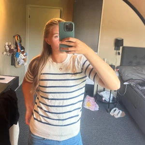 Randig vit och marinblå tröja - Säljer en fräsch vit tröja med marinblå horisontella ränder. Tröjan har korta ärmar och rund halsringning. Perfekt för dig som gillar en klassisk och stilren look. Materialet känns mjukt och skönt mot huden.