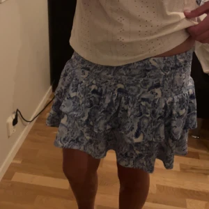 Blåvit volangkjol med mönster - Supersöt kort kjol i blått och vitt med volanger och ett abstrakt mönster. Använd endast 1 gång!