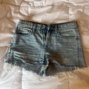 Blå jeansshorts från H&M - Snygga blå jeansshorts från H&M i Strl 36/S. Är sparsamt använda och har inga synliga defekter. Perfekta för sommaren och ger en avslappnad vibe till din outfit.