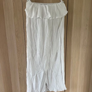 Vit offshoulder långklänning med volang - Superfin vit långklänning med offshoulder och volang upptill. Klänningen är luftig och har en lätt, flowy känsla – perfekt för varma dagar. Materialet känns tunt och svalt, och modellen är rak och enkel utan ärmar. Perfekt strandklänning!