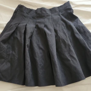 Svart kortkjol från SHEIN - Svart kortkjol från SHEIN med bred linning och snygga veck framtill som ger extra volym. Kjolen har en klassisk A-linjeform och är tillverkad i ett mjukt bomullstyg. Perfekt att matcha med en crop top eller oversized hoodie. 