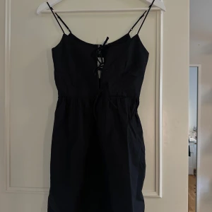 Svart kort klänning med snörning H&M - Svart kort klänning från H&M med tunna axelband och tre snöresdetaljer framtill. Säljer pågrund av att den inte kommer komma till användning.