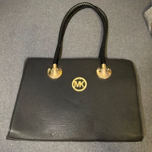 Svart handväska - Svart handväska köpt på marknaden i Spanien, guldiga detaljer och flätade handtag. Väskan har flera fack inuti och dragkedja baktill. Knappt använd. Storlek: ca 35x28x12