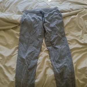 Grå mjukisbyxor från SOC med snörning - Grå mjukisbyxor från SOC med elastisk midja och svart snörning. Byxorna har en enkel och clean design med diskret logga på benet. Perfekta för chill dagar eller träning. Tillverkade i mjukt bomullsmaterial för extra komfort.